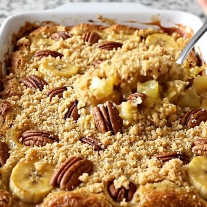 A golden-brown Hummingbird Dump Cake in a white ceramic dish with toasted pecans on top.