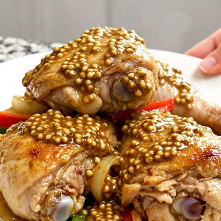 A top-down view of tender, braised chicken thighs coated in a rich, grainy Creole mustard sauce with colorful bell peppers.
