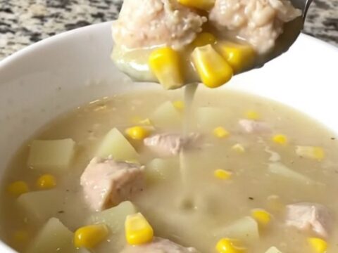 A top-down view of a black slow cooker filled with chicken, corn, potatoes, and creamy broth.
