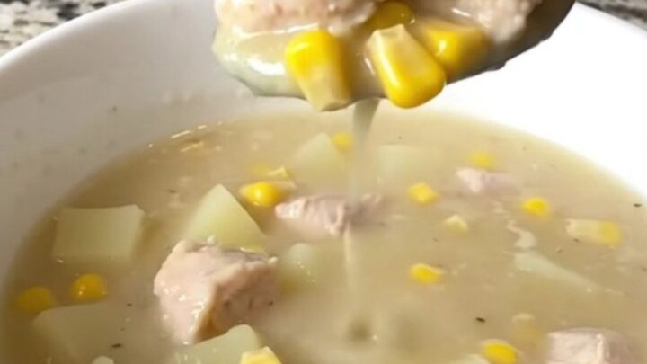 A top-down view of a black slow cooker filled with chicken, corn, potatoes, and creamy broth.