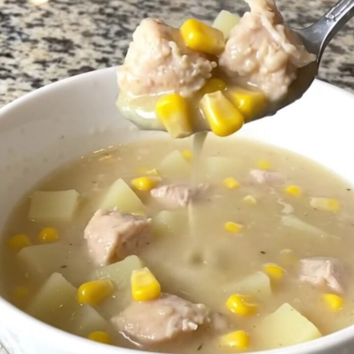 A top-down view of a black slow cooker filled with chicken, corn, potatoes, and creamy broth.