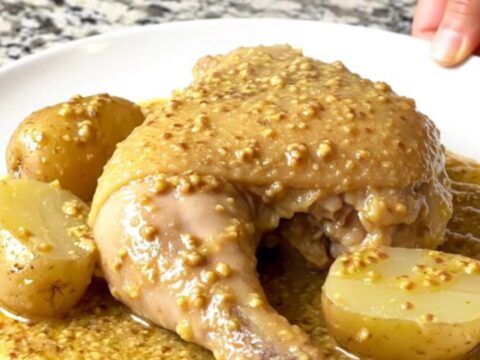 Four golden, tender chicken leg quarters and baby potatoes nestled in a creamy Dijon sauce inside a black slow cooker.