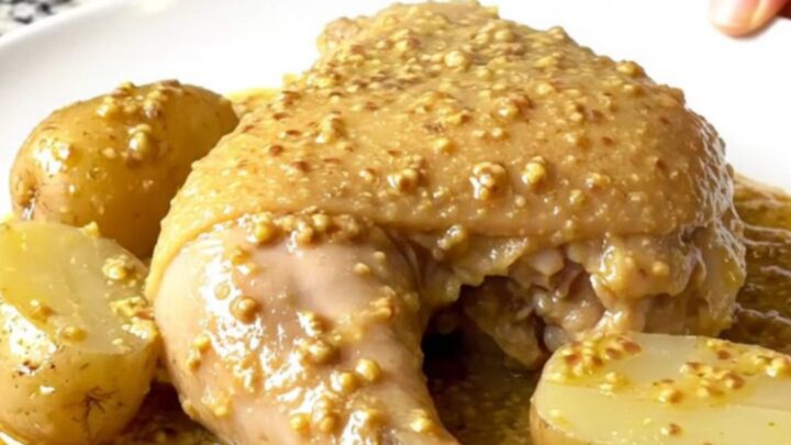 Four golden, tender chicken leg quarters and baby potatoes nestled in a creamy Dijon sauce inside a black slow cooker.