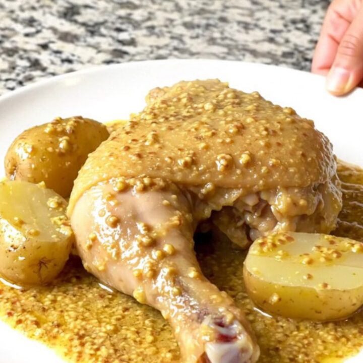 Four golden, tender chicken leg quarters and baby potatoes nestled in a creamy Dijon sauce inside a black slow cooker.