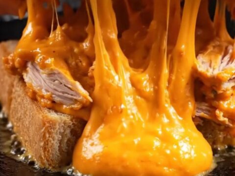 A crispy buffalo chicken melt with a golden cheese crust on golden Texas toast, featuring molten filling.