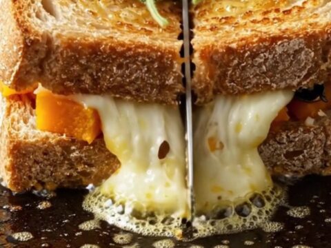A close-up of a crispy sourdough melt cut in half, showing roasted butternut squash and melted Fontina cheese inside.