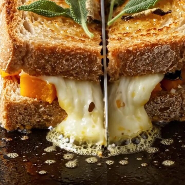 A close-up of a crispy sourdough melt cut in half, showing roasted butternut squash and melted Fontina cheese inside.