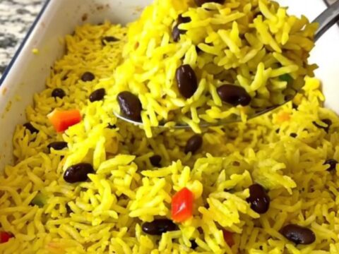 A large rectangular baker filled with colorful yellow rice, black beans, and diced bell peppers before baking.