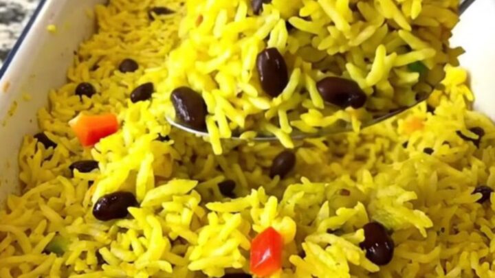 A large rectangular baker filled with colorful yellow rice, black beans, and diced bell peppers before baking.