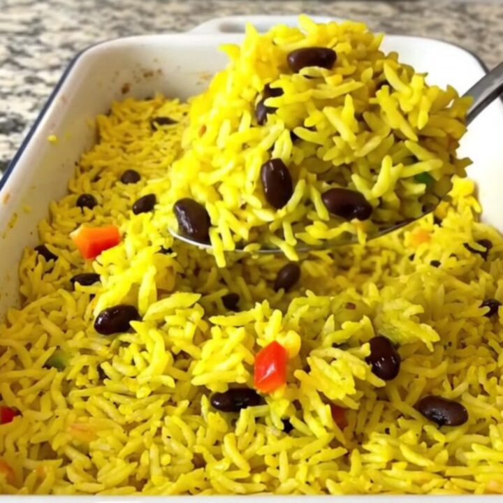 A large rectangular baker filled with colorful yellow rice, black beans, and diced bell peppers before baking.