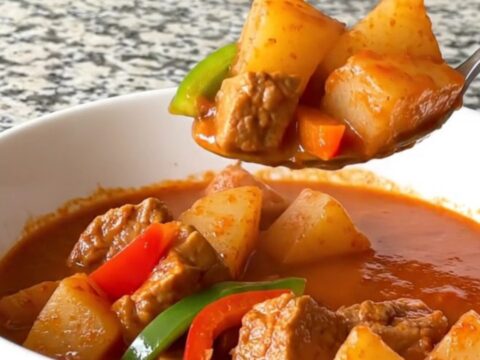 A close-up of a slow cooker filled with cubes of pork, potatoes, and peppers in a rich tomato sauce.