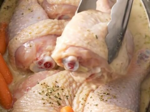 Slow cooker filled with cooked chicken leg quarters, baby carrots, and creamy ranch sauce.
