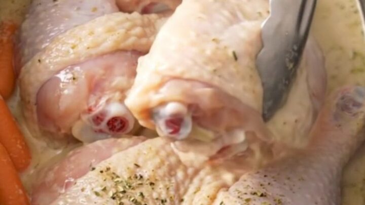 Slow cooker filled with cooked chicken leg quarters, baby carrots, and creamy ranch sauce.