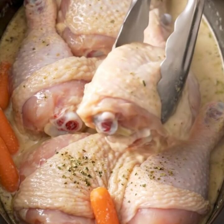 Slow cooker filled with cooked chicken leg quarters, baby carrots, and creamy ranch sauce.