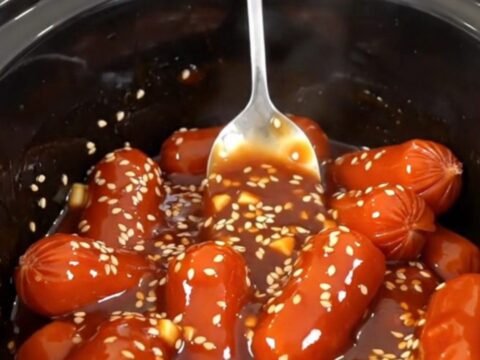 A close-up of honey gochujang cocktail sausages in a slow cooker, glistening with a thick, spicy-sweet glaze.