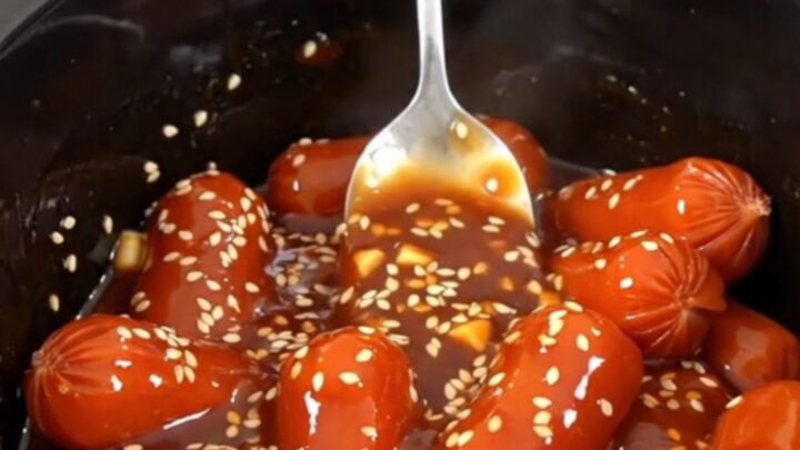 A close-up of honey gochujang cocktail sausages in a slow cooker, glistening with a thick, spicy-sweet glaze.