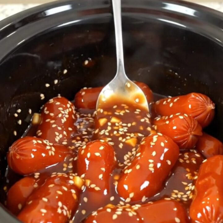 A close-up of honey gochujang cocktail sausages in a slow cooker, glistening with a thick, spicy-sweet glaze.