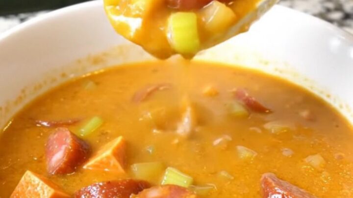 A top-down view of a black slow cooker filled with a creamy Cajun chowder containing andouille sausage and sweet potatoes.