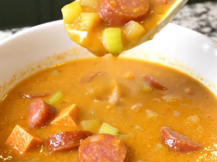 A top-down view of a black slow cooker filled with a creamy Cajun chowder containing andouille sausage and sweet potatoes.