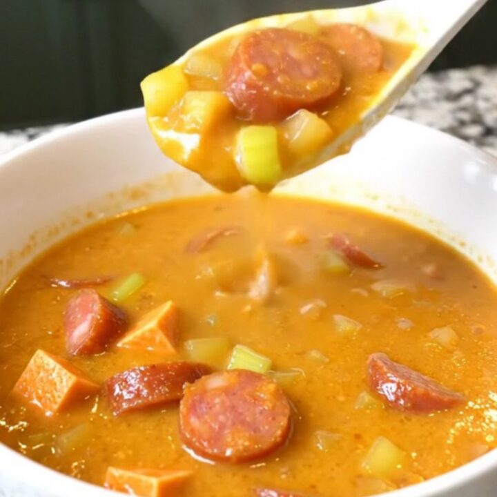 A top-down view of a black slow cooker filled with a creamy Cajun chowder containing andouille sausage and sweet potatoes.
