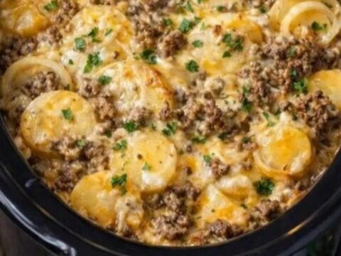 A serving spoon scooping up a portion of hot, bubbly slow cooker beef and potato au gratin with melted cheese pulls.