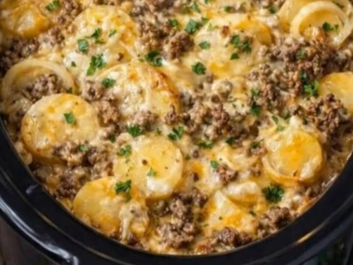 A serving spoon scooping up a portion of hot, bubbly slow cooker beef and potato au gratin with melted cheese pulls.