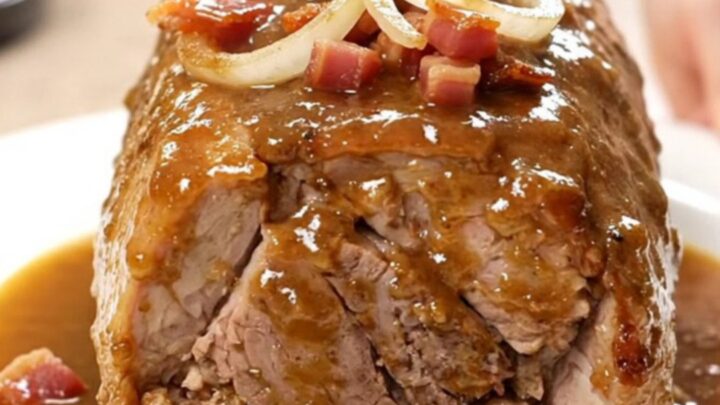 Slow cooker pork loin topped with bacon and onions, served on a white plate.