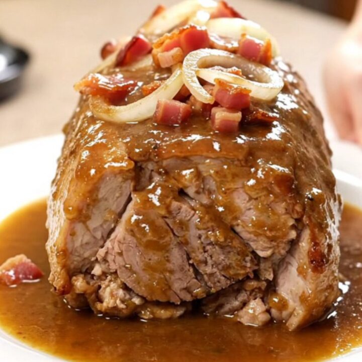Slow cooker pork loin topped with bacon and onions, served on a white plate.