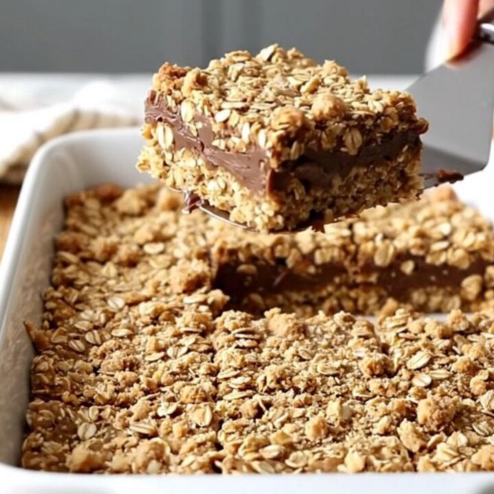 A top-down view of oatmeal fudge revel bars in a white ceramic baking dish on a butcher-block counter.