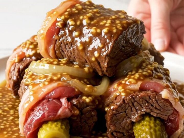 A top-down view of six raw beef rouladen rolls stuffed with bacon and pickles inside a black slow cooker.