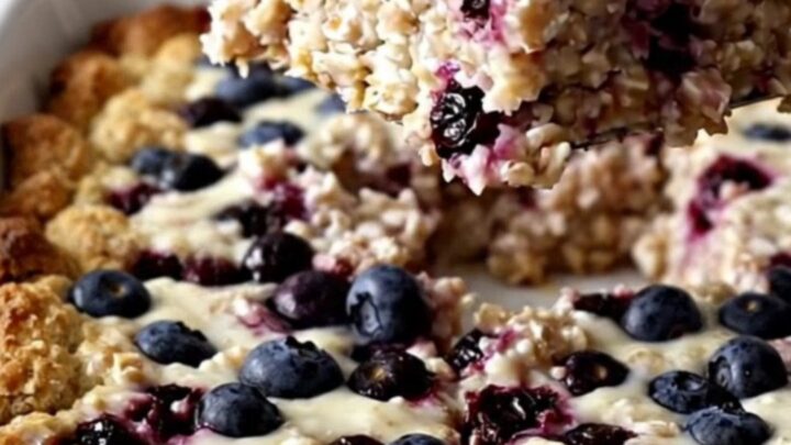 A rectangular dish of golden-brown baked oatmeal with visible blueberries on a white surface.