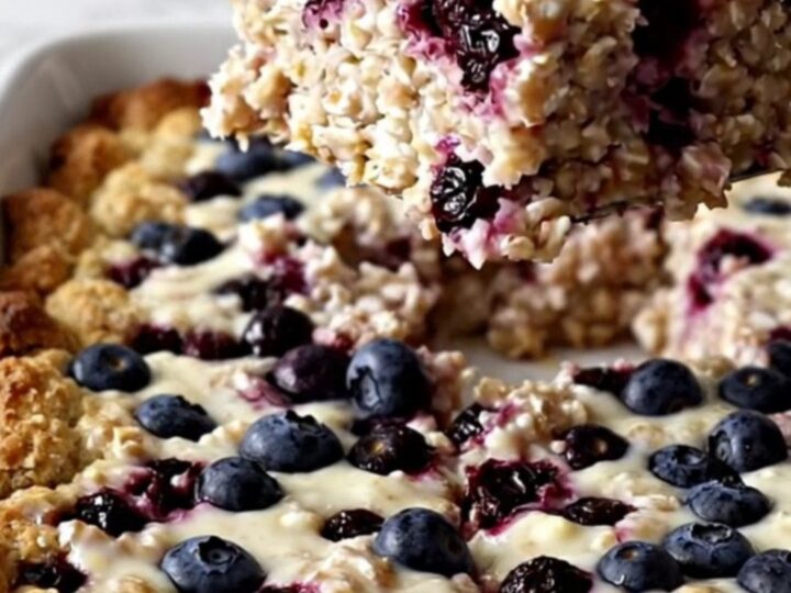 A rectangular dish of golden-brown baked oatmeal with visible blueberries on a white surface.