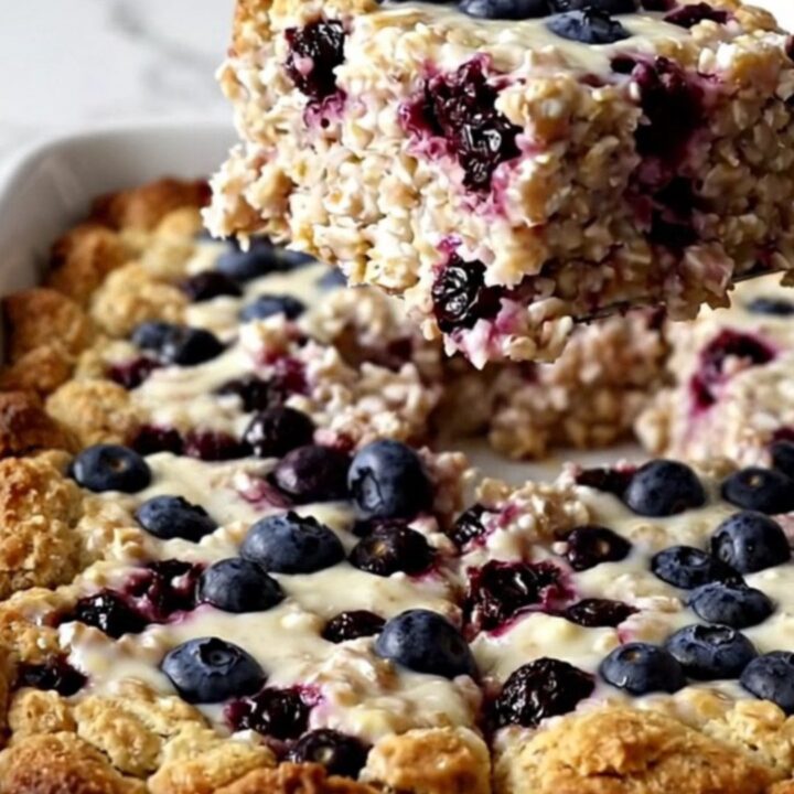 A rectangular dish of golden-brown baked oatmeal with visible blueberries on a white surface.