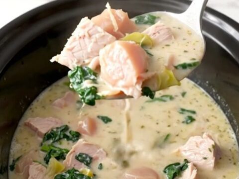 A bowl of creamy turkey spinach artichoke soup, garnished with parmesan, served in a white bowl on a dark table.