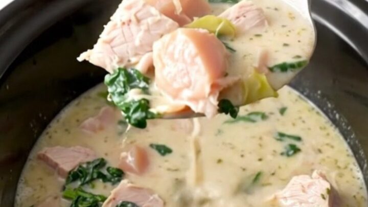 A bowl of creamy turkey spinach artichoke soup, garnished with parmesan, served in a white bowl on a dark table.