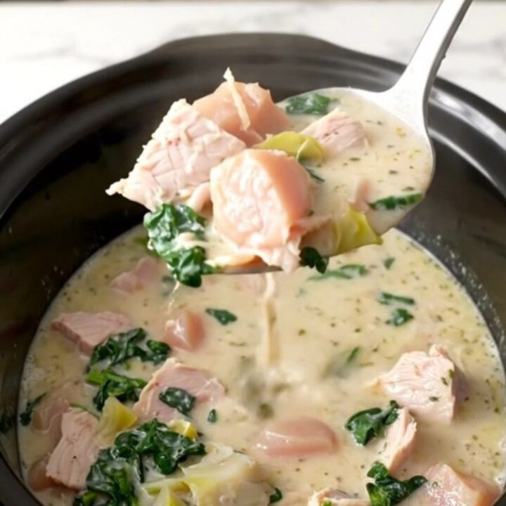 A bowl of creamy turkey spinach artichoke soup, garnished with parmesan, served in a white bowl on a dark table.
