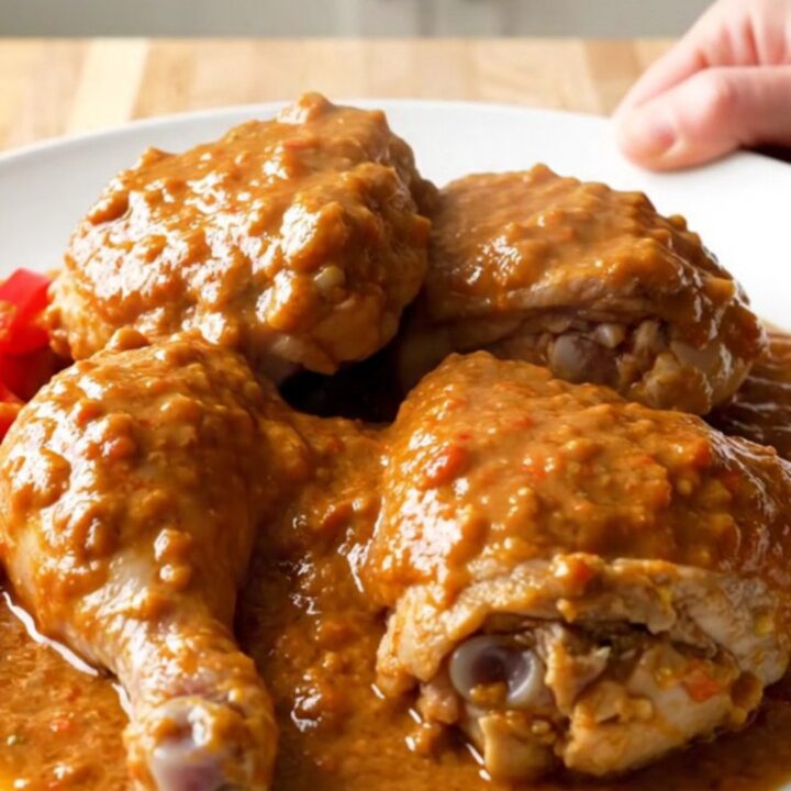 A close-up of tender chicken thighs covered in a thick, creamy peanut tomato sauce in a white slow cooker.