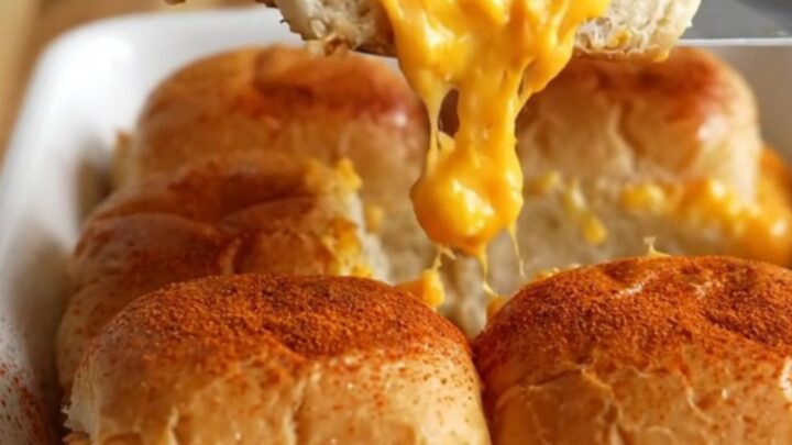 A close-up of golden-brown sliders in a white ceramic dish, with visible melted pimento cheese and ham.