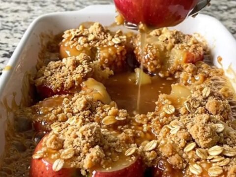 A rectangular ceramic dish filled with golden baked apple halves topped with a crunchy oat crumble.