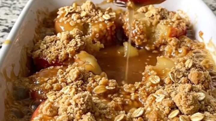 A rectangular ceramic dish filled with golden baked apple halves topped with a crunchy oat crumble.