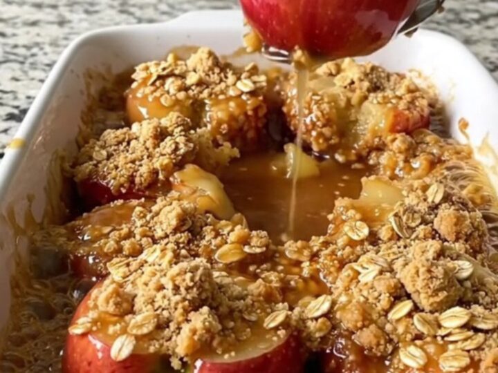 A rectangular ceramic dish filled with golden baked apple halves topped with a crunchy oat crumble.