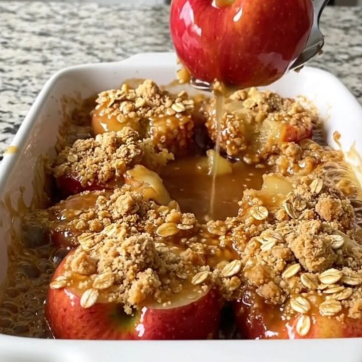 A rectangular ceramic dish filled with golden baked apple halves topped with a crunchy oat crumble.