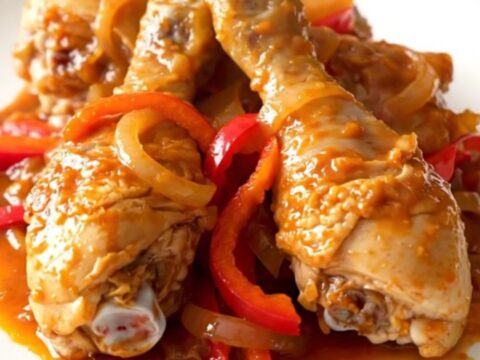 A slow cooker filled with peri peri chicken drumsticks, sliced red peppers, and onions in a vibrant red sauce.