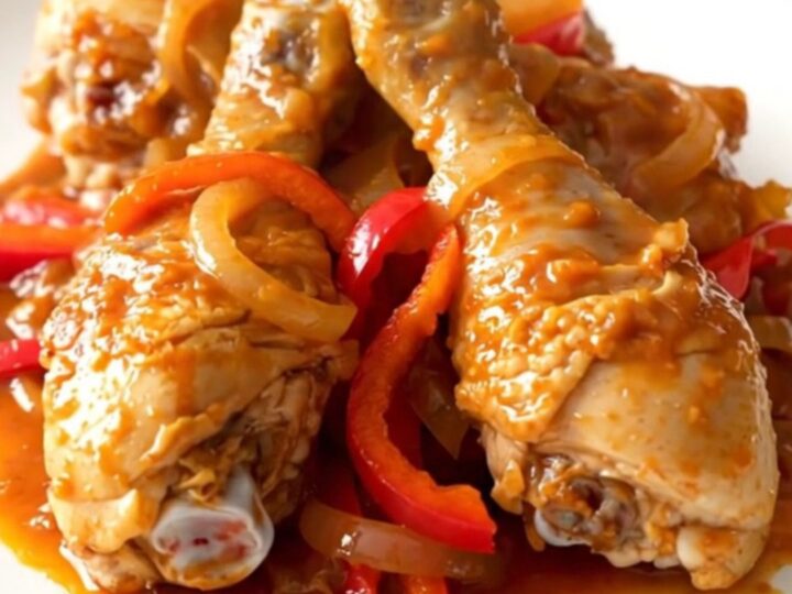 A slow cooker filled with peri peri chicken drumsticks, sliced red peppers, and onions in a vibrant red sauce.