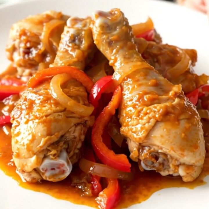 A slow cooker filled with peri peri chicken drumsticks, sliced red peppers, and onions in a vibrant red sauce.