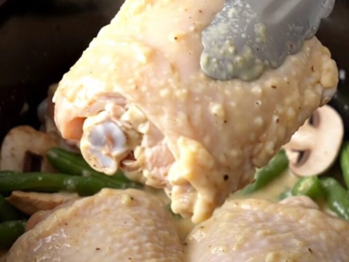 A close-up of creamy ranch mushroom chicken thighs with green beans in a black slow cooker insert.