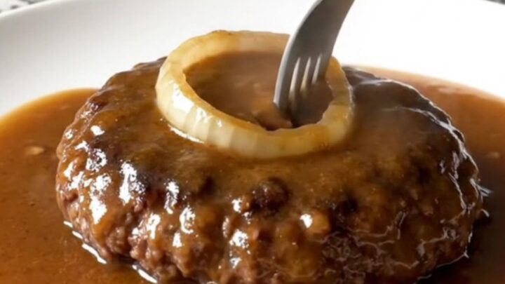 A plate featuring a tender, brown hamburger steak covered in a thick, savory onion gravy.