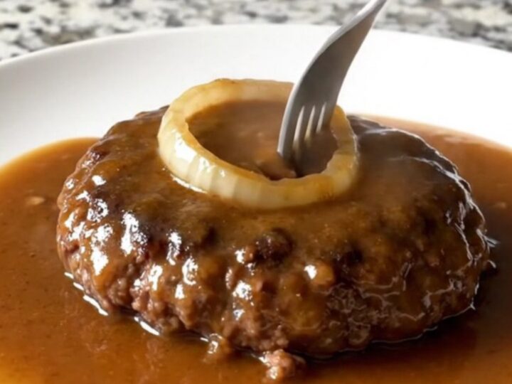 A plate featuring a tender, brown hamburger steak covered in a thick, savory onion gravy.