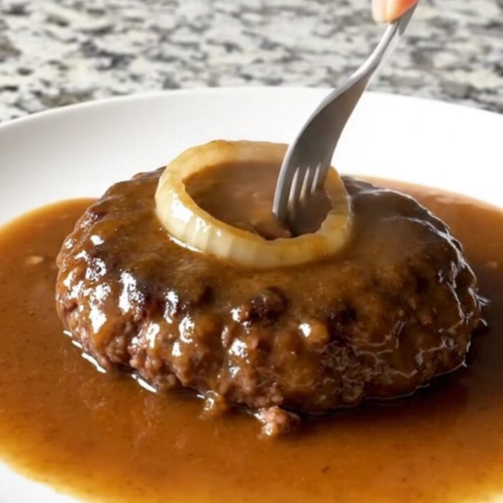 A plate featuring a tender, brown hamburger steak covered in a thick, savory onion gravy.