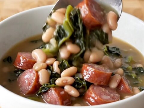 A hearty bowl of Southern swamp stew featuring sausage coins, white beans, and dark greens in a rich broth.